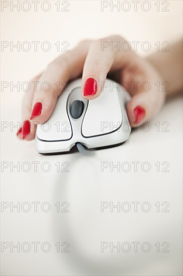 Close up of woman's hand with red nail polish holding computer mouse.