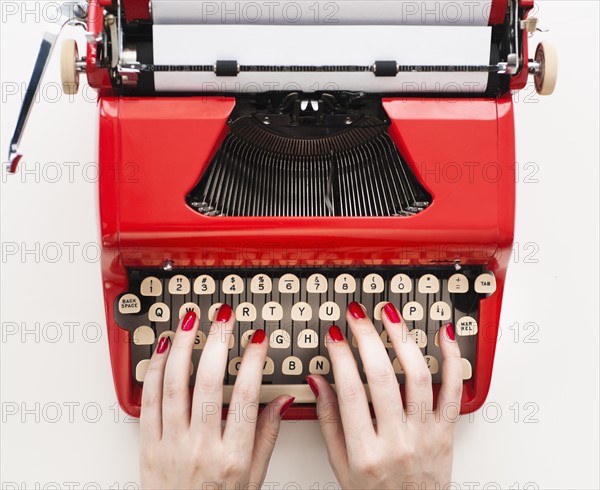 Close up of woman's hands with red nail polish typing on antique typewriter.