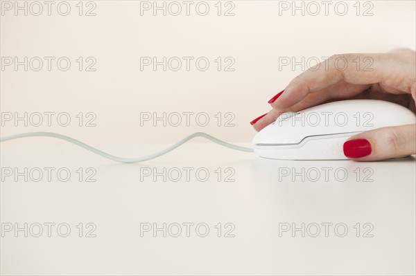 Close up of woman's hand with red nail polish holding computer mouse.