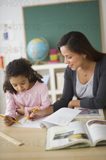 Girl (6-7) with female teacher sitting at desk in classroom.