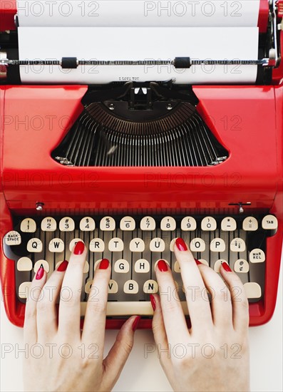 Close up of woman's hands with red nail polish typing on antique typewriter.