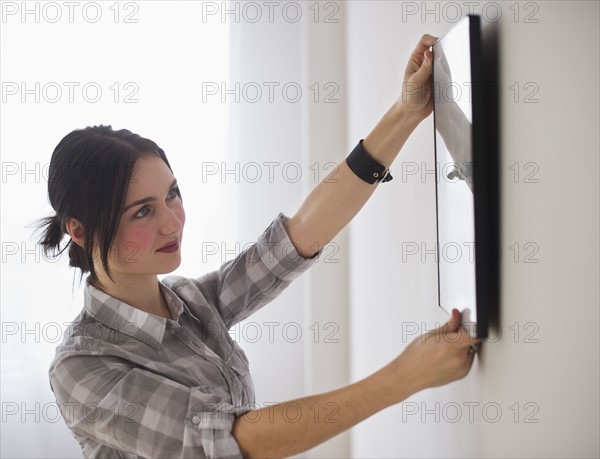 Woman hanging picture on wall. Photo: Daniel Grill