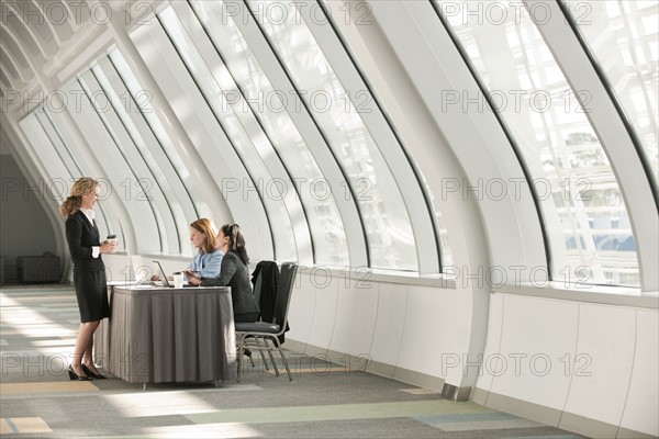 Businesswomen talking at desk in corridor. Photo: Mark Edward Atkinson