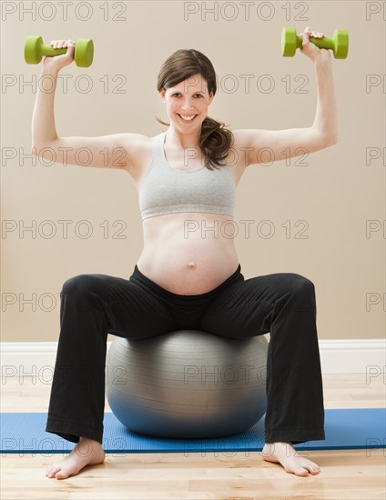 Young pregnant woman exercising with dumbbells and fitness ball. Photo : Mike Kemp