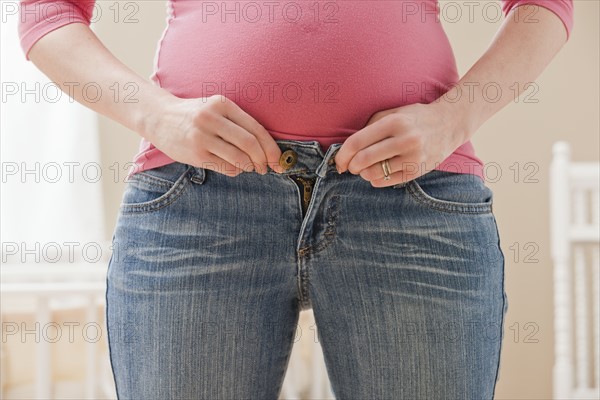 Young pregnant woman buttoning jeans. Photo : Mike Kemp