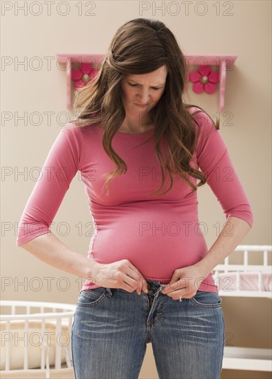 Young pregnant woman buttoning jeans. Photo : Mike Kemp