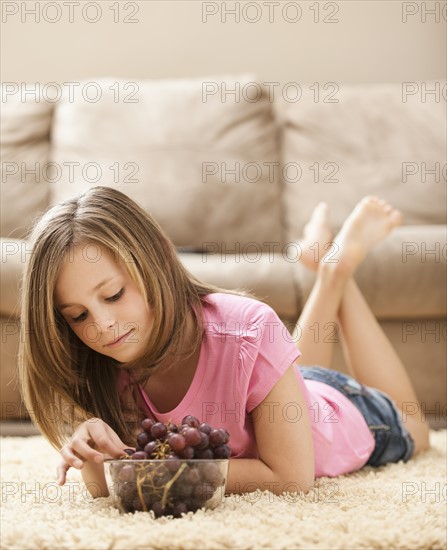 Girl (10-11) lying on floor eating grapes. Photo : Mike Kemp