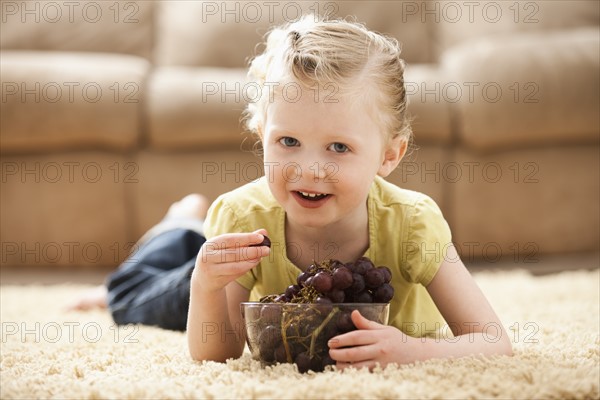 Girl (2-3) lying on floor eating grapes. Photo: Mike Kemp