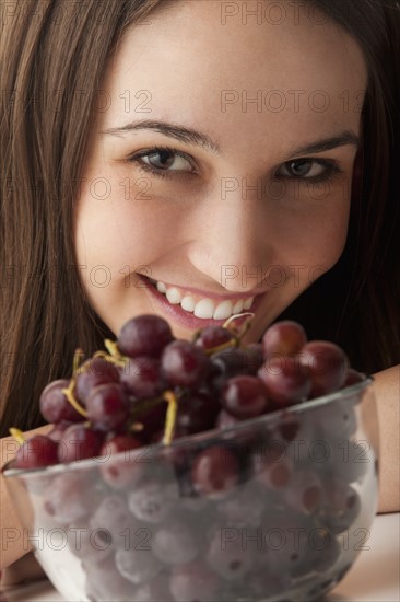Studio portrait of young woman with grapes. Photo : Mike Kemp