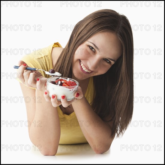 Studio portrait of young woman eating strawberries and yogurt. Photo : Mike Kemp