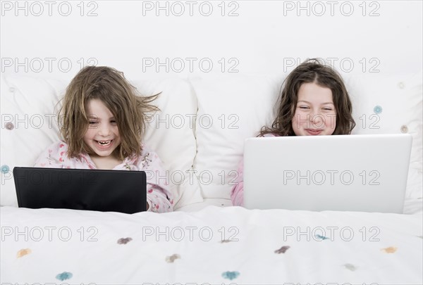 Girls (6-7,8-9) with laptops sitting in bed. Photo: Justin Paget