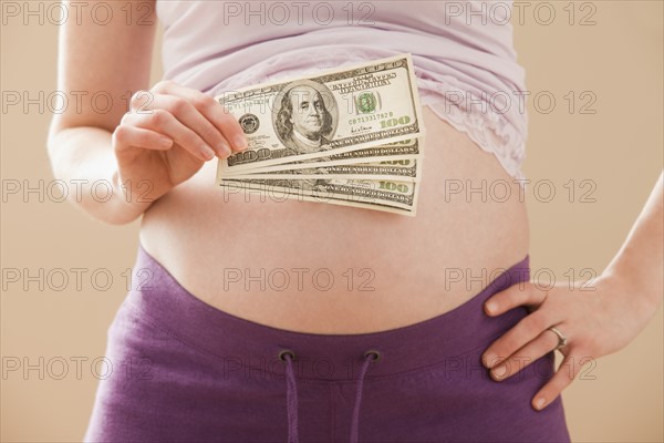 Young pregnant woman holding money roll of dollars. Photo: Mike Kemp