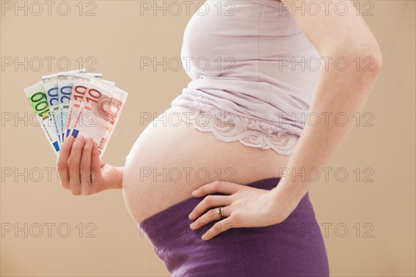 Young pregnant woman holding money roll of Euros. Photo: Mike Kemp