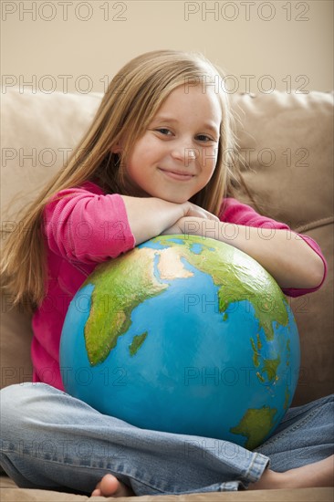 Cheerful girl (8-9) sitting on sofa with globe on knees. Photo : Mike Kemp