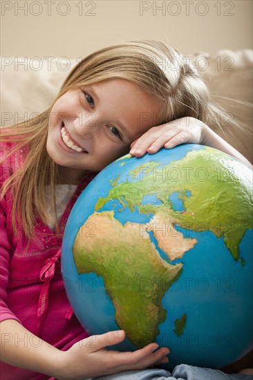 Cheerful girl (8-9) sitting on sofa with globe on knees. Photo : Mike Kemp