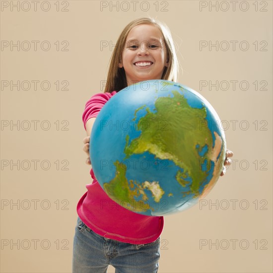 Studio portrait of girl (8-9) holding globe. Photo : Mike Kemp