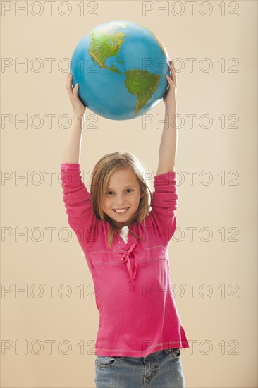 Studio portrait of girl (8-9) holding globe. Photo : Mike Kemp