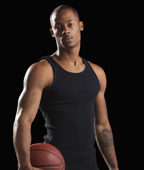 Studio portrait of young man with basketball. Photo : Mike Kemp