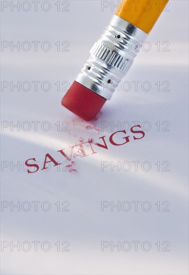 Studio shot of pencil erasing the word savings from piece of paper. Photo : Daniel Grill