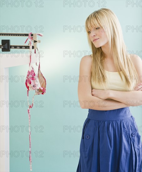 Woman looking at bikini hanging on weight scale. Photo: Jamie Grill Photography
