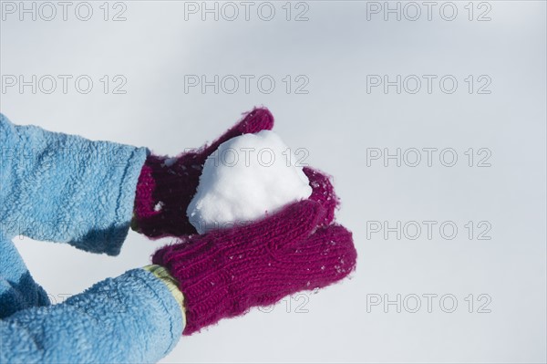 Close up of girl's (6-7) hands in mittens holding snowball.