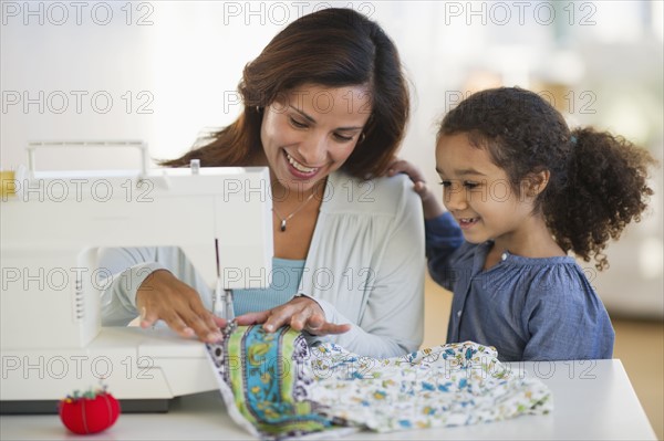 Mother with daughter (6-7) using sewing machine.