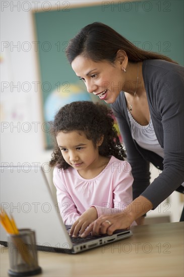 Girl (6-7) with female teacher using laptop in classroom.