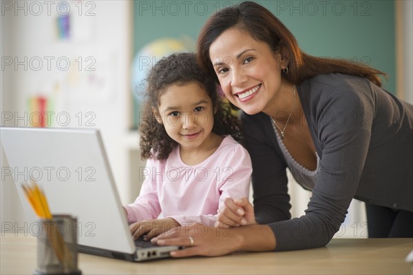 Girl (6-7) with female teacher using laptop in classroom.