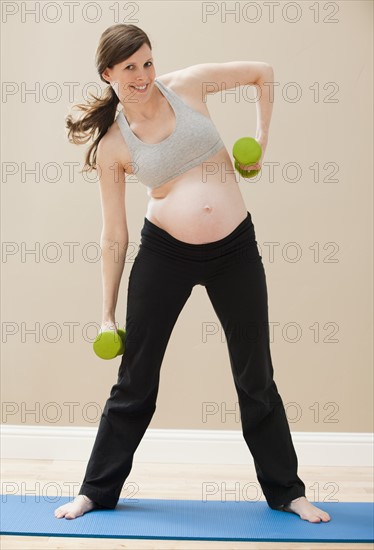 Young pregnant woman exercising with dumbbells. Photo : Mike Kemp