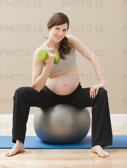 Young pregnant woman exercising with dumbbells and fitness ball. Photo : Mike Kemp