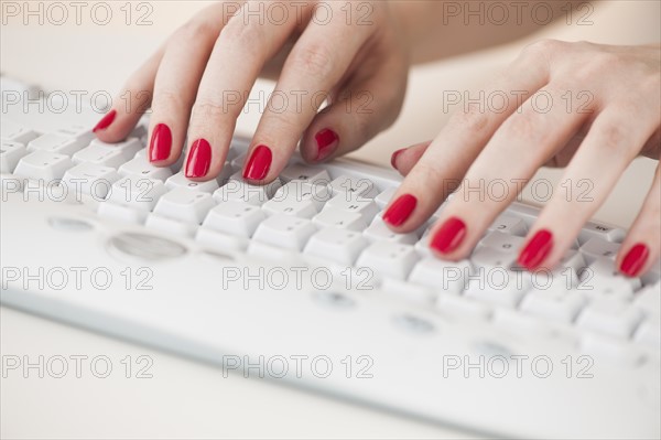 Close up of woman's fingers with red nail polish typing on computer keyboard.