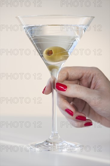 Close up of woman's hand with nail polish holding martini glass with olive.