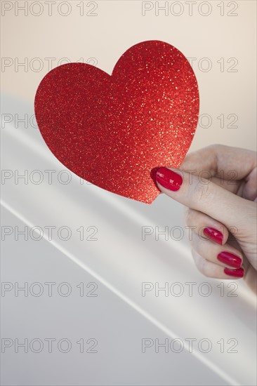 Close up of woman's fingers with red nail polish holding red heart.