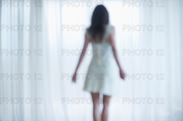 Young woman standing and looking through window.