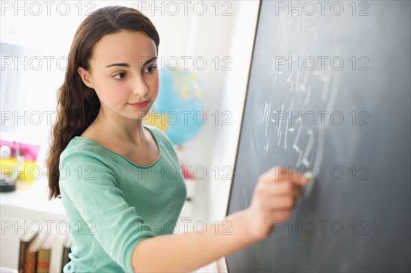 Teenage girl (14-15) writing on blackboard.