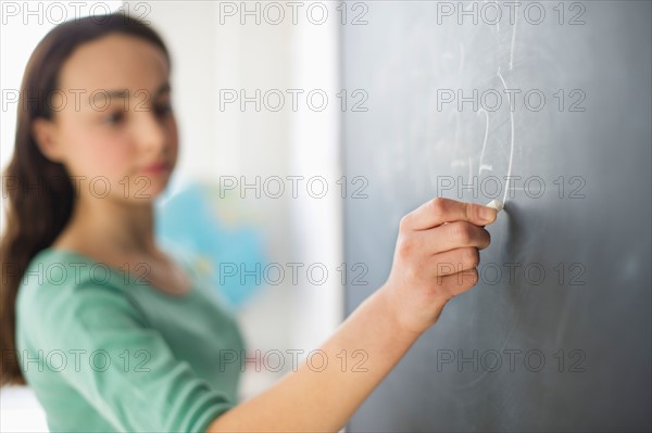 Teenage girl (14-15) writing on blackboard.