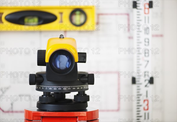 Still life with blueprints and level, theodolite on foreground.