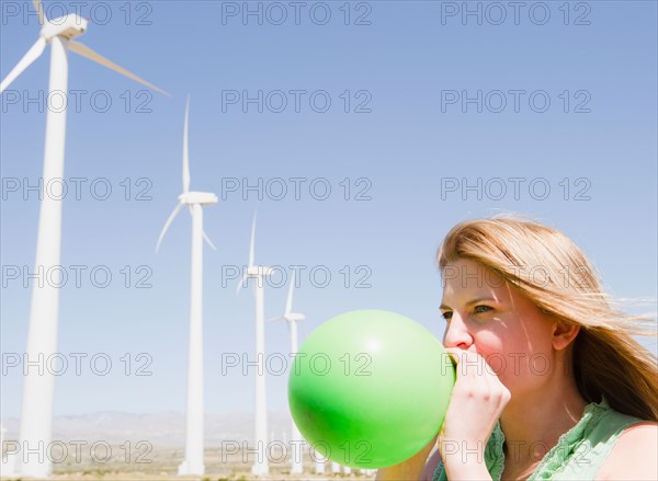 USA, California, Palm Springs, Coachella Valley, San Gorgonio Pass, Woman blowing green balloon with wind turbines in background. Photo : Jamie Grill Photography