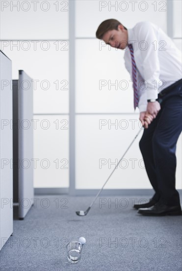 Businessman playing golf at office. Photo : Daniel Grill