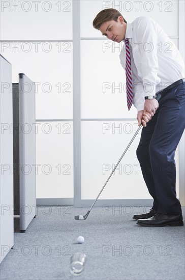 Businessman playing golf at office. Photo : Daniel Grill