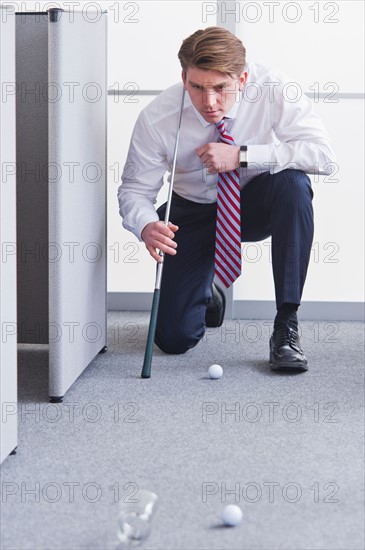 Businessman playing golf at office. Photo : Daniel Grill