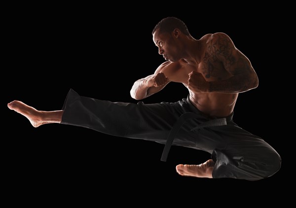 Studio shot of martial arts practitioner in mid-air kick. Photo : Mike Kemp