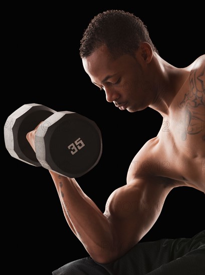 Studio shot of muscular man exercising with dumbbells. Photo : Mike Kemp