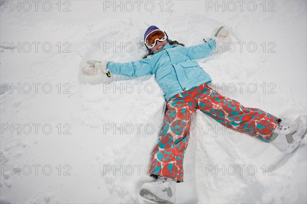 Girl (10-11) in ski gear doing snow angel. Photo : db2stock