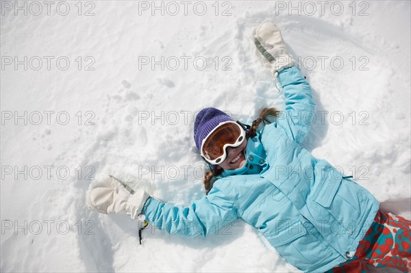 Girl (10-11) in ski gear doing snow angel. Photo : db2stock