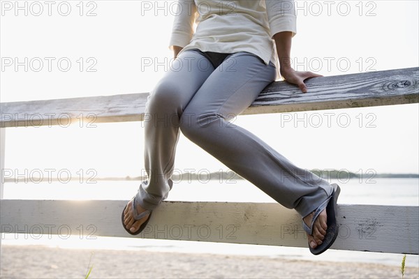 Legs of woman sitting on rail fence, lake in background. Photo : Maisie Paterson