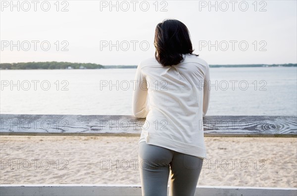 USA, New York State, Long Island, woman leaning against rail fence and looking at lake. Photo : Maisie Paterson