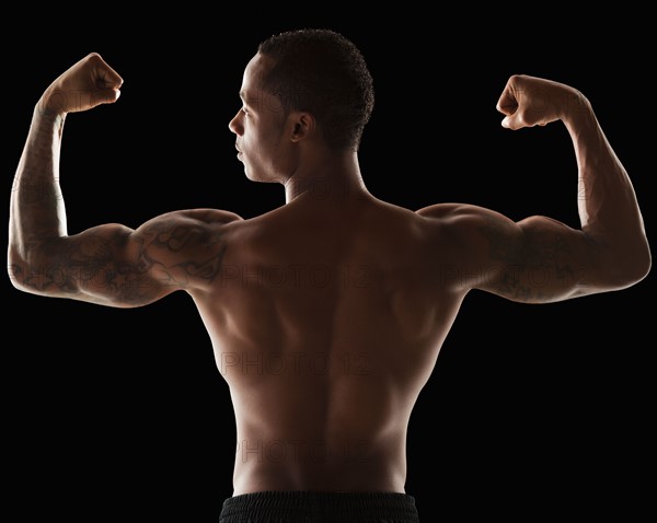 Rear view of muscular man flexing muscles. Photo : Mike Kemp