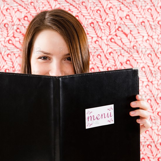 Portrait of smiling young woman holding restaurant menu in front of face. Photo : Jamie Grill Photography
