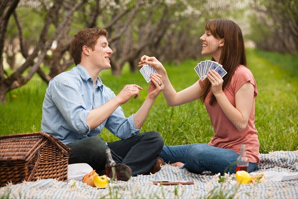 USA, Utah, Provo, Young couple playing cards during picnic in orchard. Photo : Mike Kemp